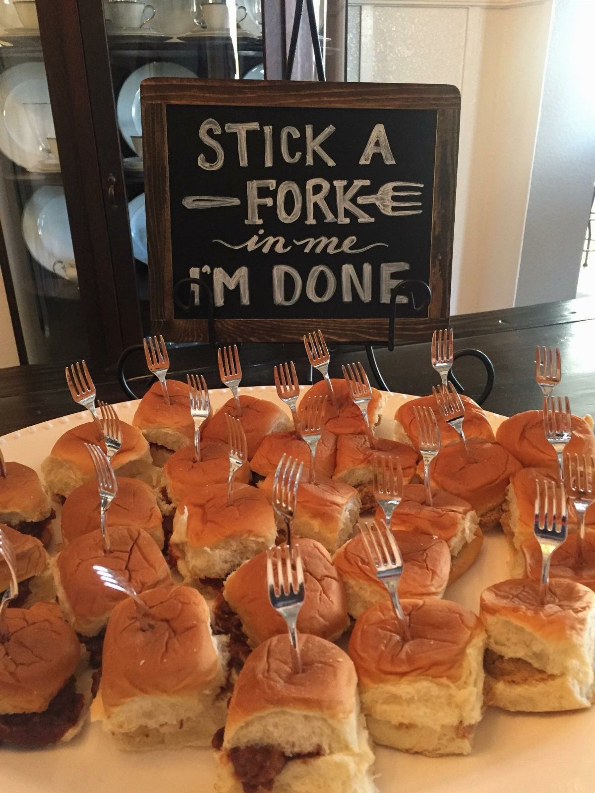 Small sliders on a white platter with plastic forks and a humorous retirement chalkboard sign.