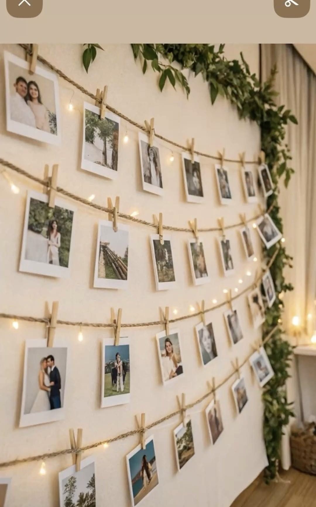 Polaroid photographs clipped to twine strings with fairy lights and green vines on a wall.