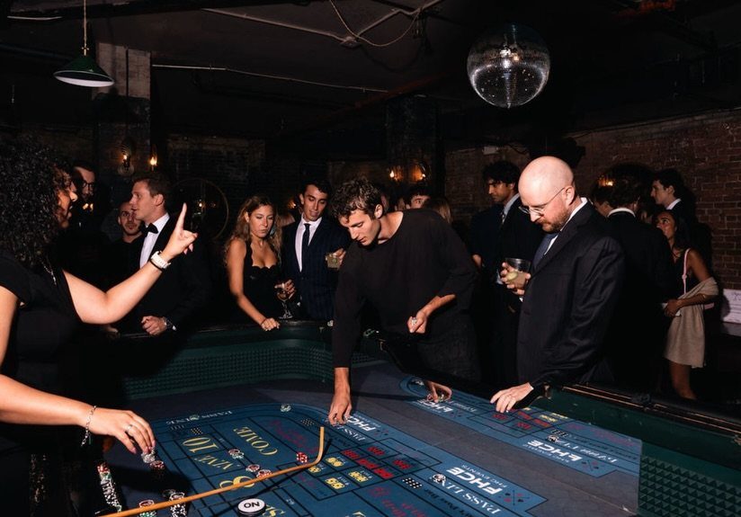People in formal wear gathered around a craps table playing dice in a dark room.