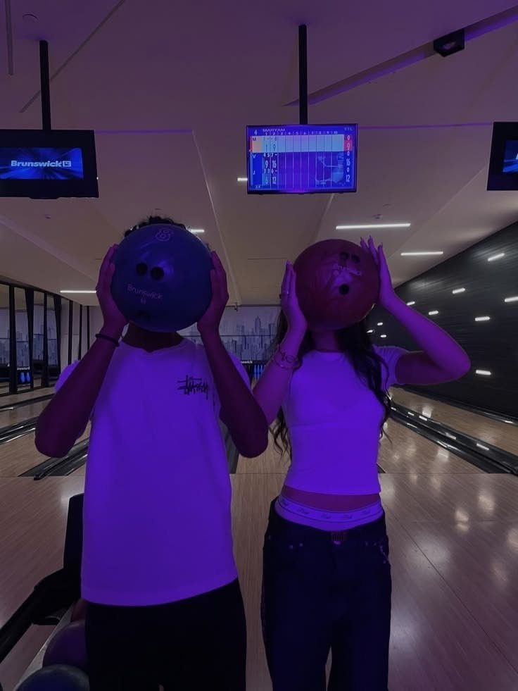 Two friends posing with bowling balls in a dimly lit bowling alley.