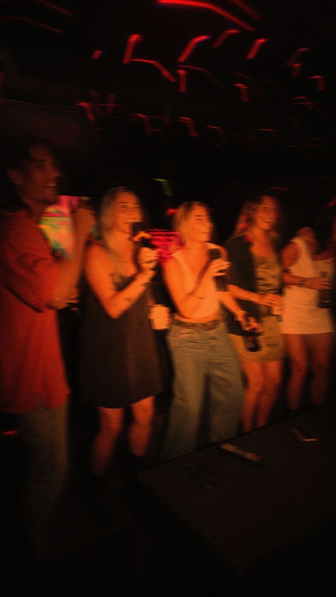 Group of friends singing karaoke on stage with microphones.