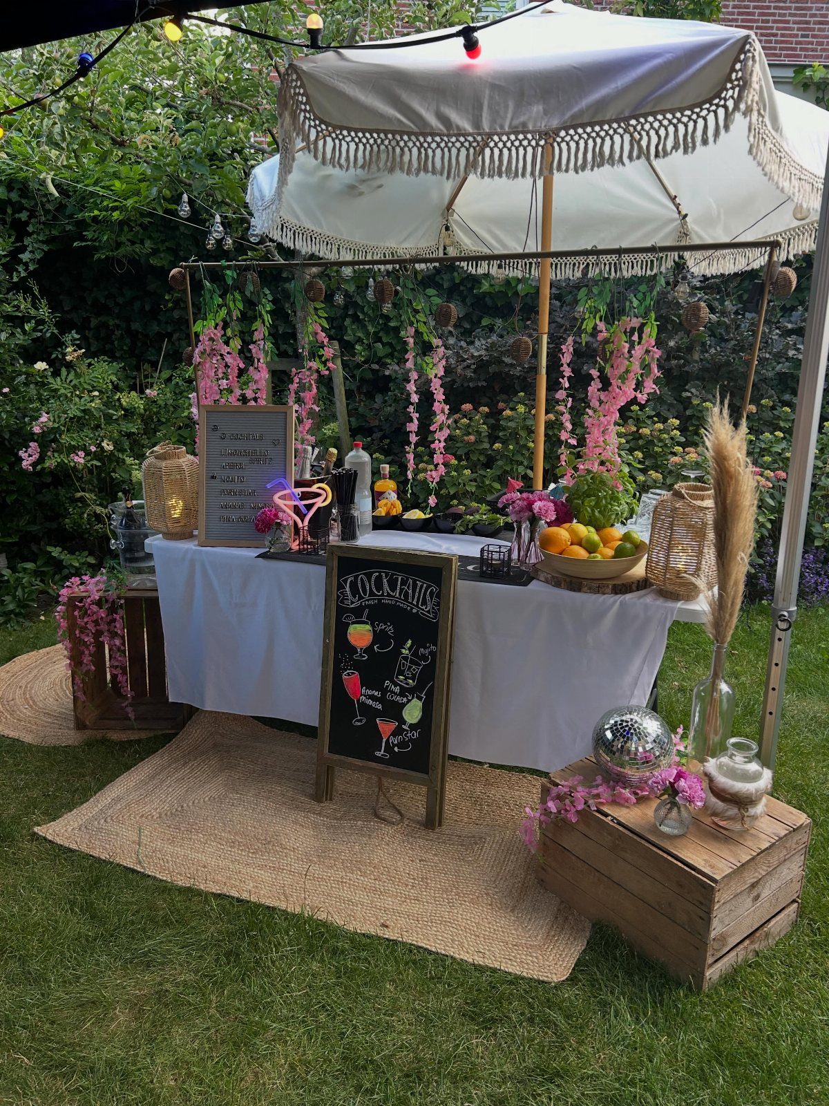Picnic setup with a table, flowers, fruits, and drinks under an umbrella.
