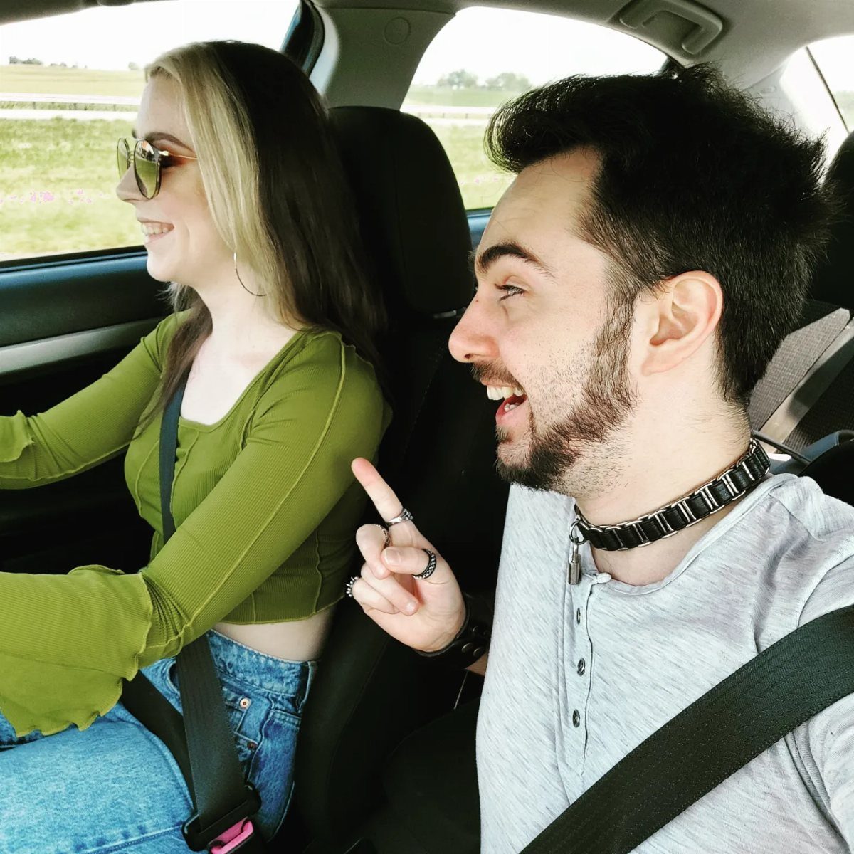 Two young adults laughing together while sitting inside a moving car.
