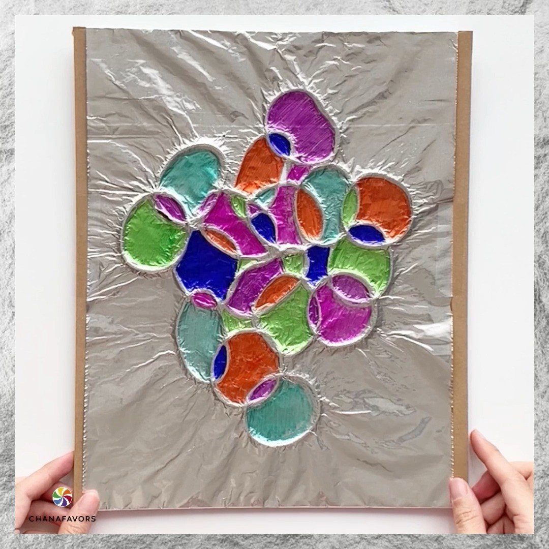 Hands holding a piece of colorful abstract art made with silver foil and translucent shapes.