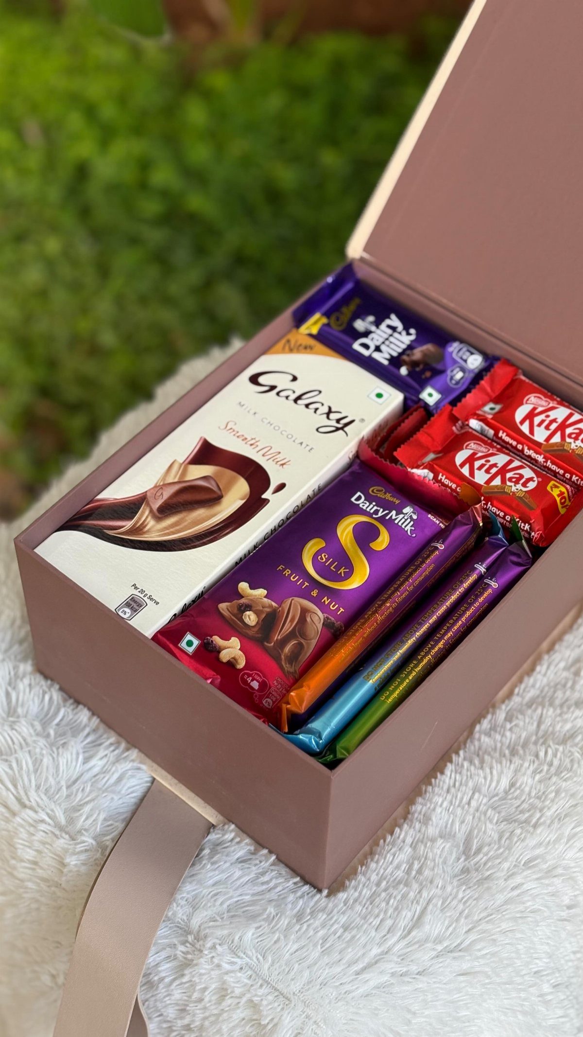 An open mauve gift box filled with various branded chocolate bars on white fluff.