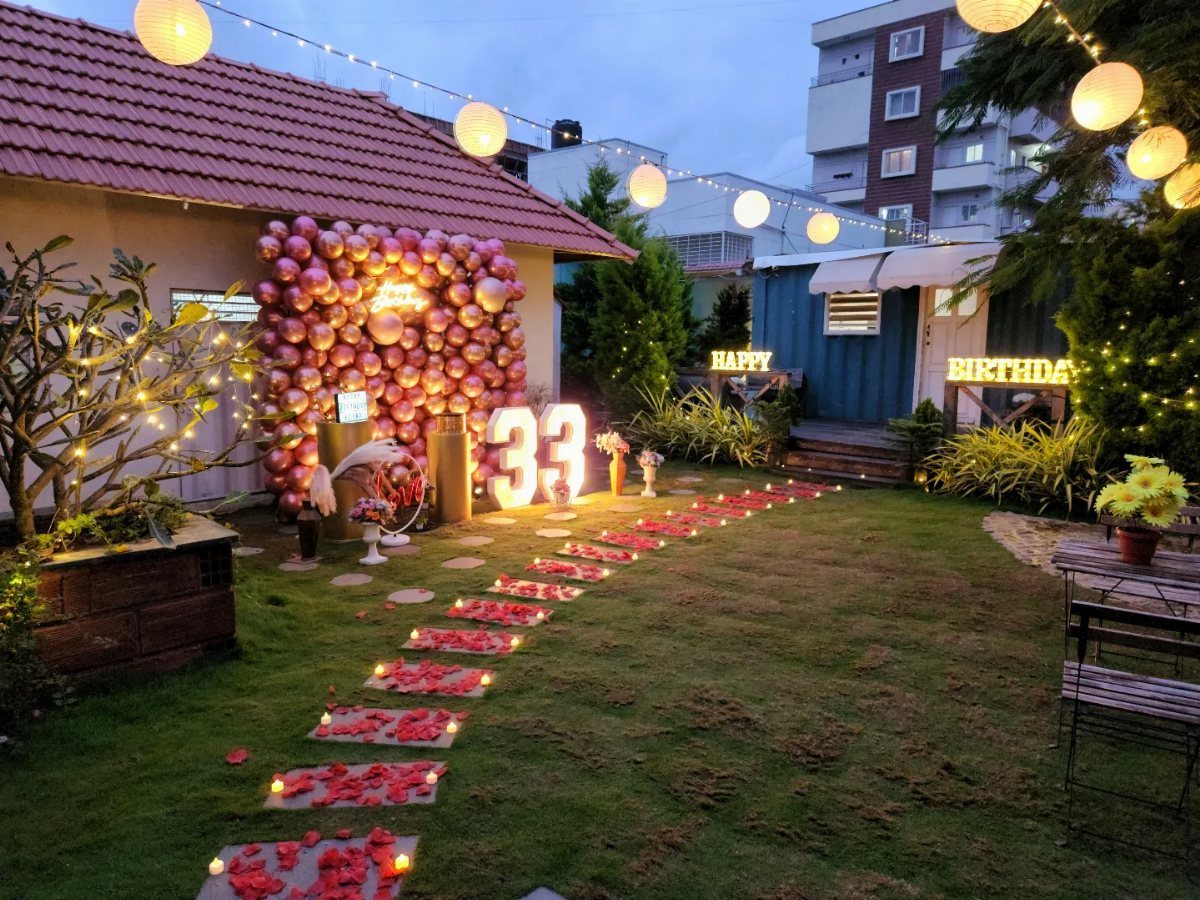 Outdoor birthday celebration setup with pink balloons, illuminated numbers, and rose petal path.