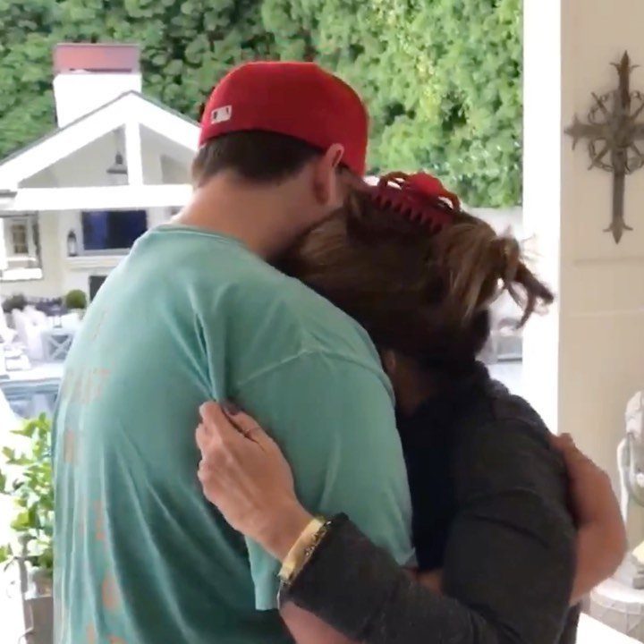 A man in a red cap and blue shirt receiving a warm, emotional hug from a woman.