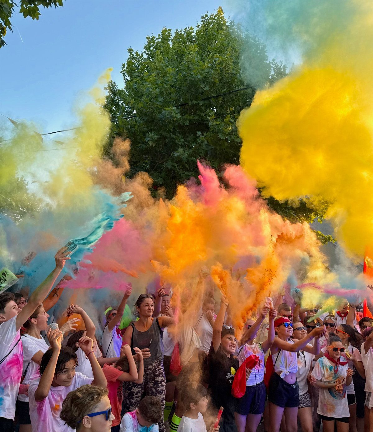 A crowd of people throwing colorful powder into the air during a vibrant outdoor celebration.