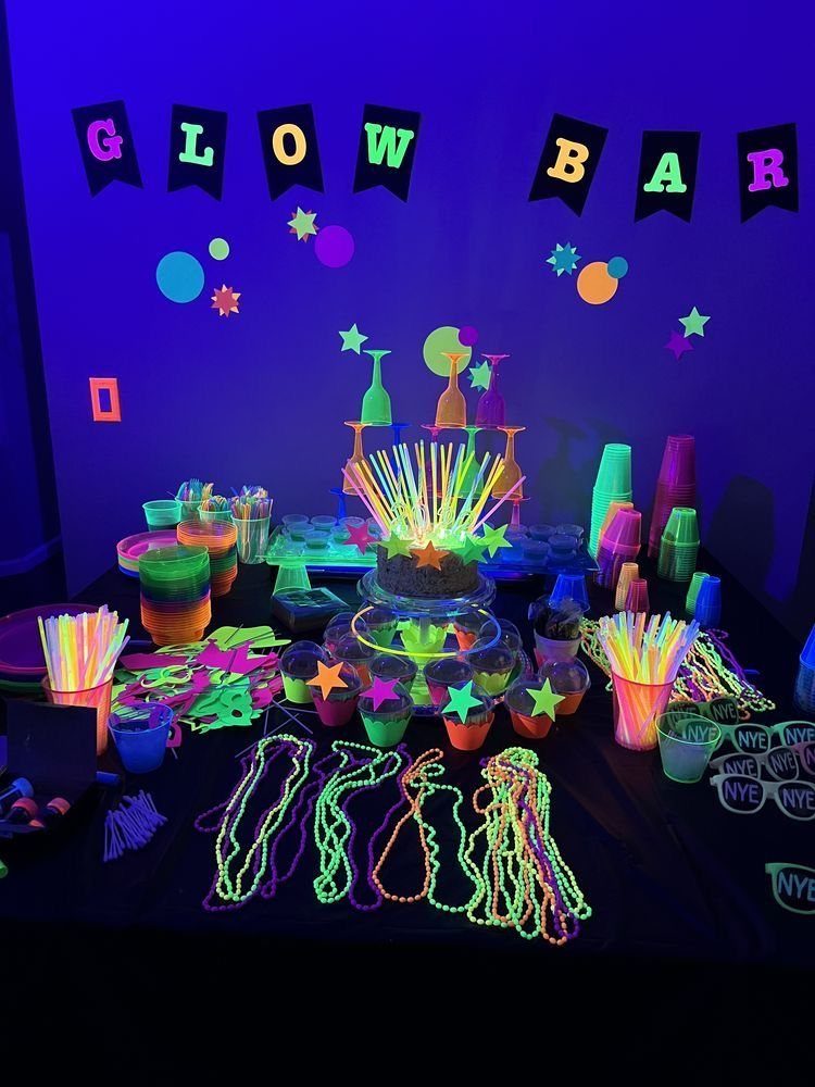 A table decorated with neon cups, straws, and beads under UV light.