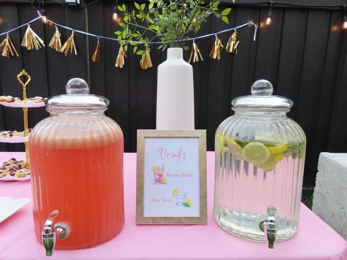 Two glass beverage dispensers filled with pink and lemon water on a pink tablecloth.