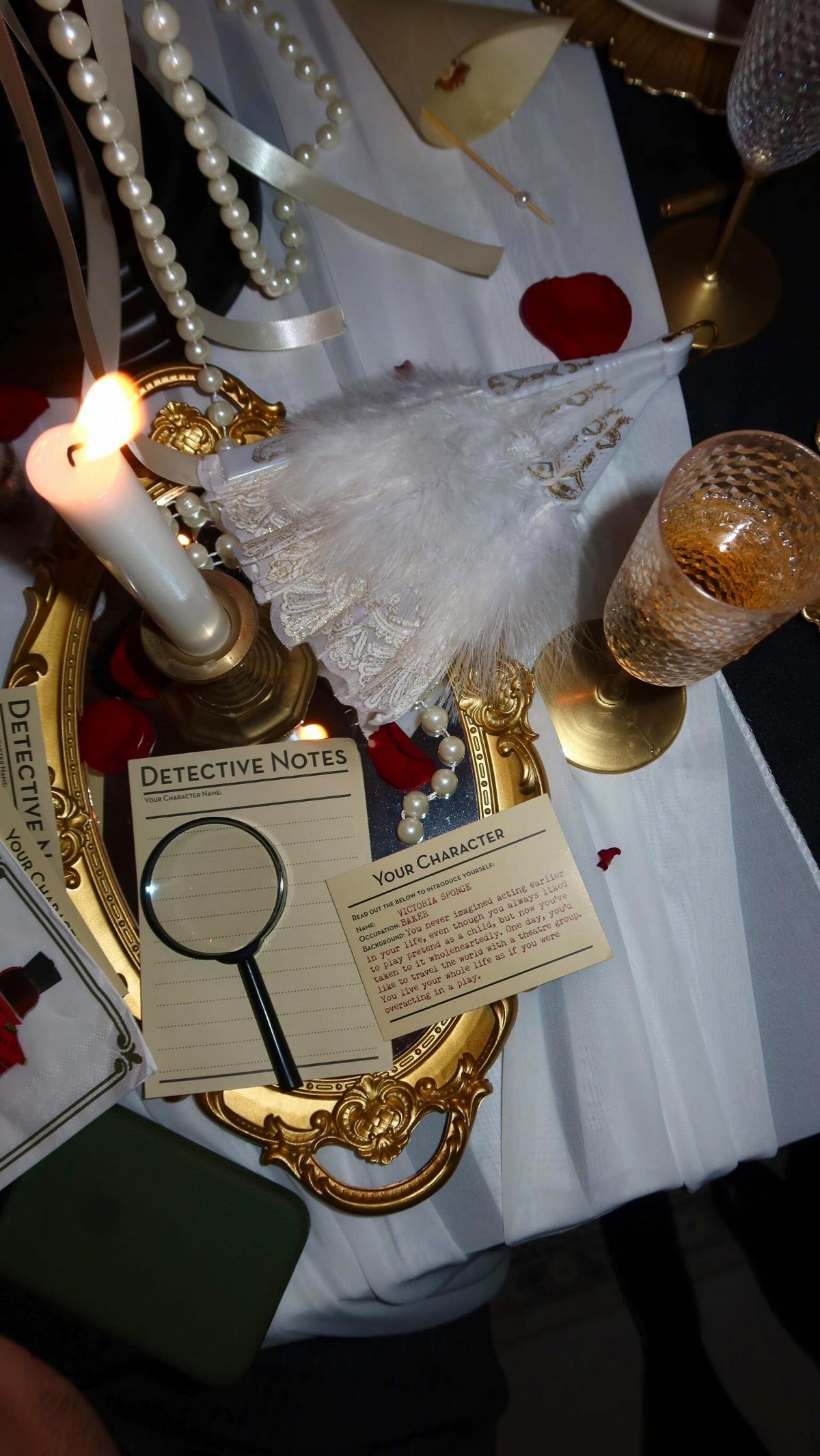 Detective notes and a magnifying glass resting on a gold tray with pearls and lace.